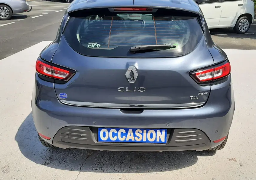 Vue arrière d'une Renault Clio IV gris titanium avec logo et feux LED, plaque "OCCASION" visible en parking.
