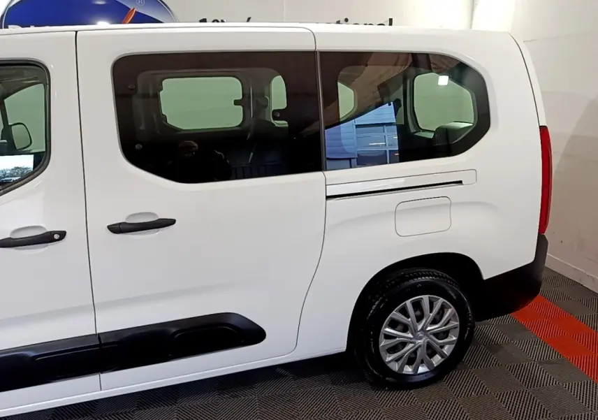 Vue latérale droite d'un Citroën Berlingo XL blanc, mettant en valeur les grandes fenêtres teintées et les protections noires sur les portières.