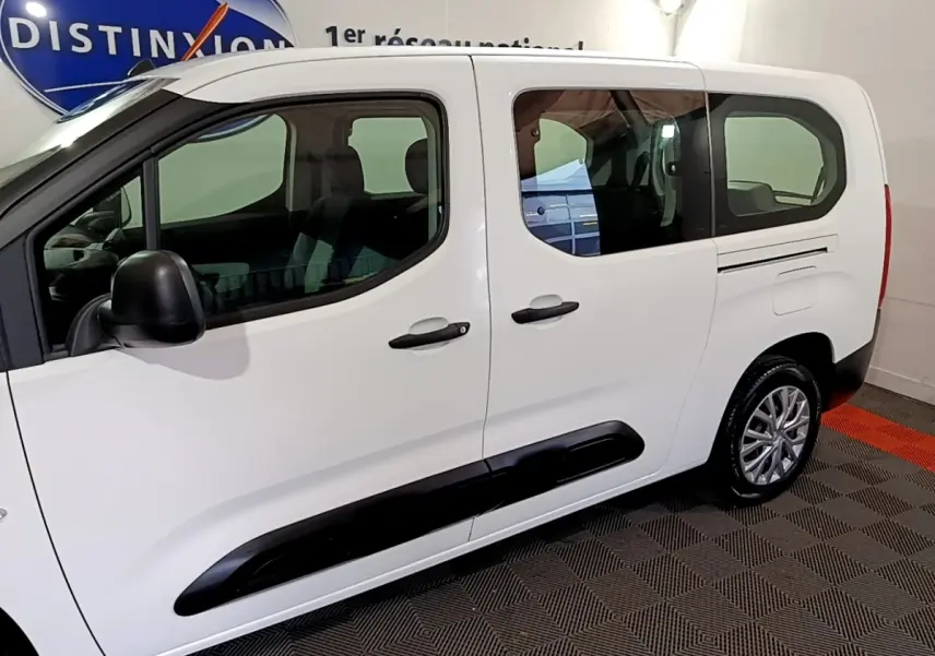 Vue de profil côté gauche d’un Citroën Berlingo XL blanc avec protections latérales noires en intérieur showroom.