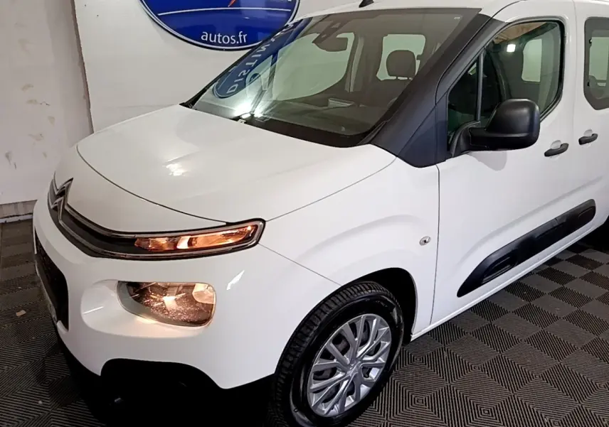Vue 3/4 avant droit d'un Citroën Berlingo XL blanc avec phares allumés et protections latérales noires.