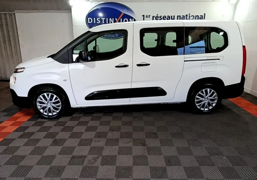 Vue de profil côté gauche d’un Citroën Berlingo XL blanc avec protections noires et jantes alliage en intérieur showroom.