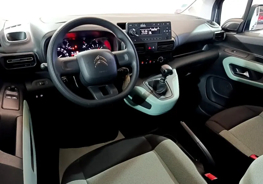 Vue intérieure côté conducteur du Citroën Berlingo blanc, avec volant, tableau de bord et levier de vitesses manuelle visibles.