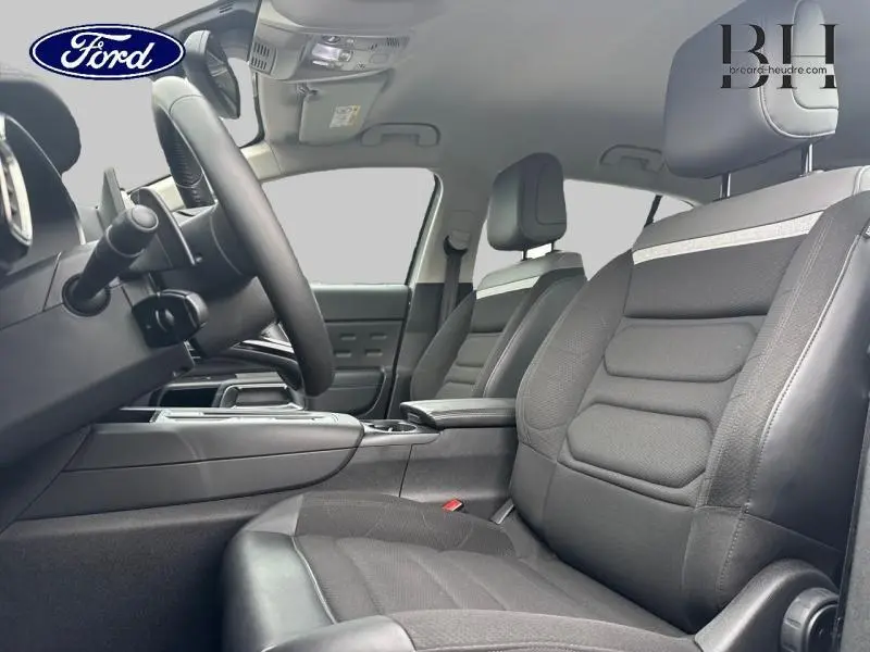 Vue intérieure côté conducteur du Citroën C5 Aircross gris acier, mettant en valeur les sièges en tissu et cuir avec accoudoir central.