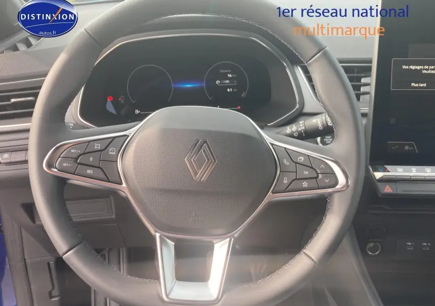 Vue rapprochée du volant multifonction noir du Renault Captur bleu iron, avec tableau de bord numérique et écran tactile visible.