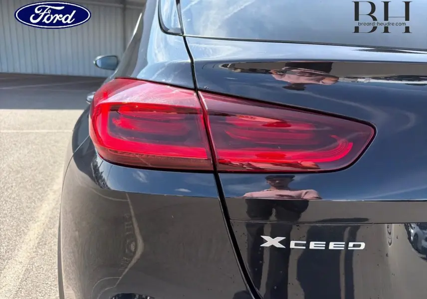 Gros plan sur le feu arrière gauche d'un KIA Xceed noir Basalte métallisé, avec logo et reflet sur la carrosserie.
