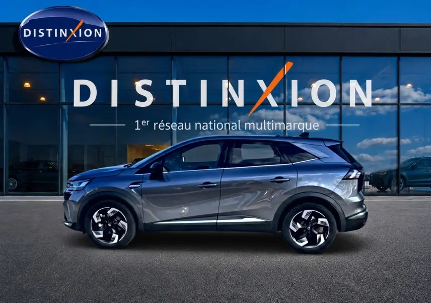 Renault Symbioz gris en profil droit devant une vitrine Distinxion, avec jantes noires et toit surélevé.