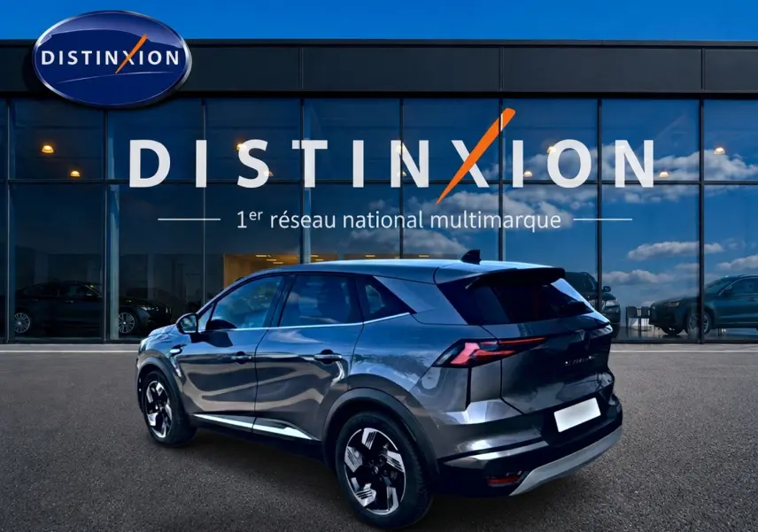 Renault Symbioz gris en 3/4 arrière droit, avec jantes noires et toit noir devant une vitrine Distinxion.