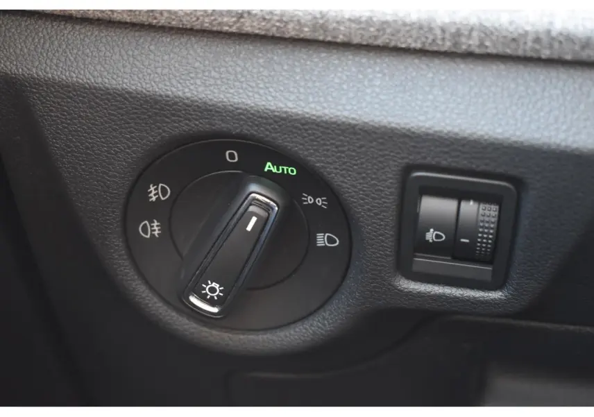Gros plan sur le bouton de commande des phares avec réglage automatique dans l'habitacle noir d'une Skoda Scala.