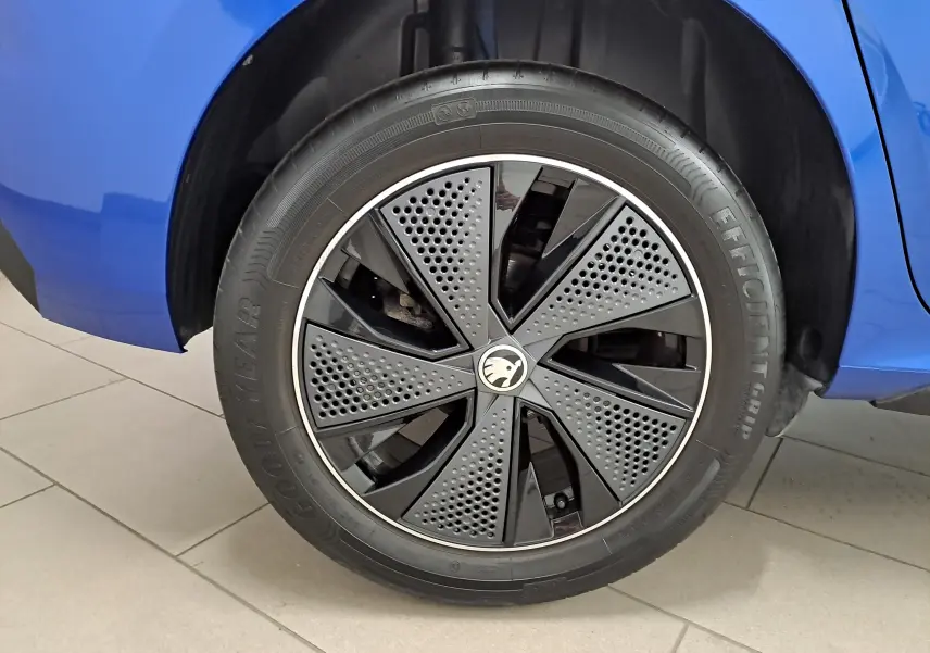 Gros plan sur la roue avant droite d’un Skoda Kamiq bleu RS, jante noire à motifs perforés et logo central visible.