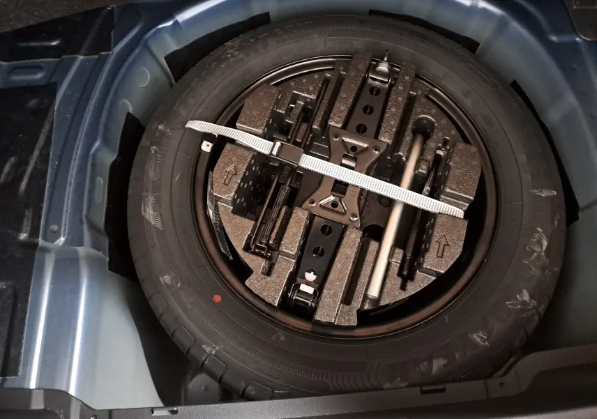 Gros plan sur la roue de secours et les outils de bord dans le double plancher du coffre bleu RS du Skoda Kamiq 2024.