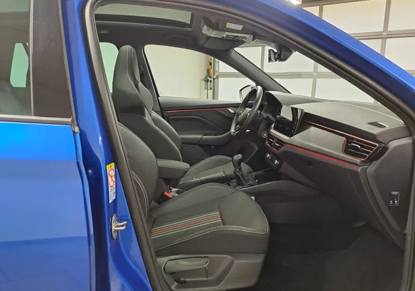 Vue intérieure côté conducteur du Skoda Kamiq Bleu RS 2024, avec sièges sport noirs et détails rouges sur le tableau de bord.