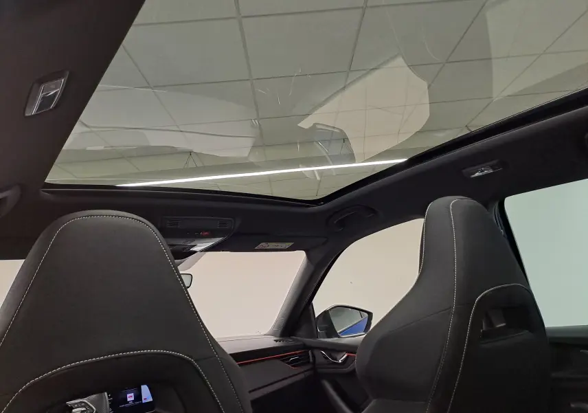 Vue intérieure du toit panoramique et des sièges avant noirs avec surpiqûres blanches du Skoda Kamiq 2024 Bleu RS.