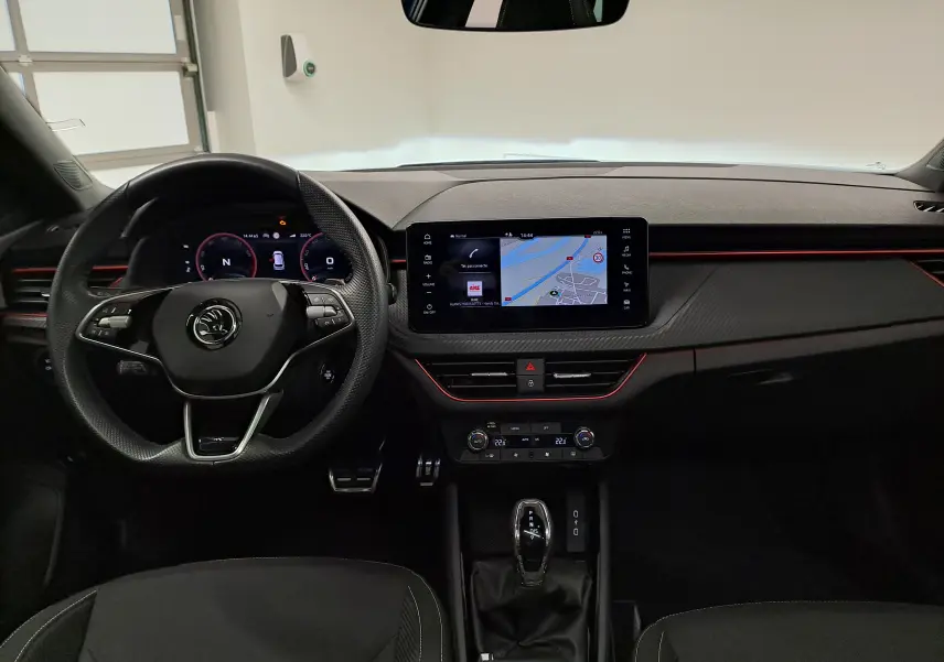 Vue intérieure frontale du Skoda Kamiq 2024, tableau de bord noir avec éclairage rouge et écran tactile central affichant la navigation.