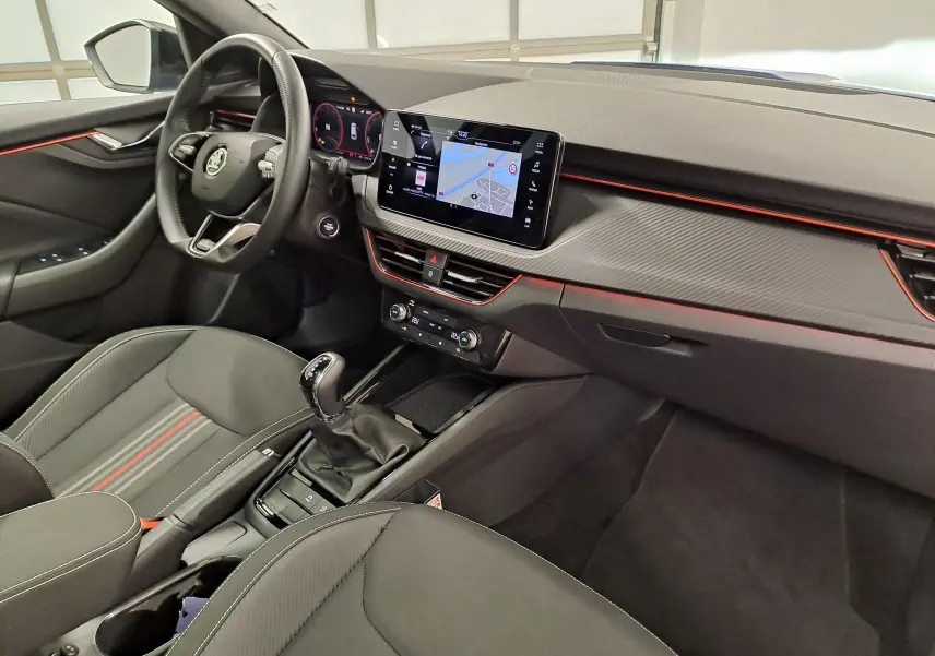 Vue intérieure côté conducteur du Skoda Kamiq 2024 avec tableau de bord noir, écran tactile central et détails rouges d'ambiance.
