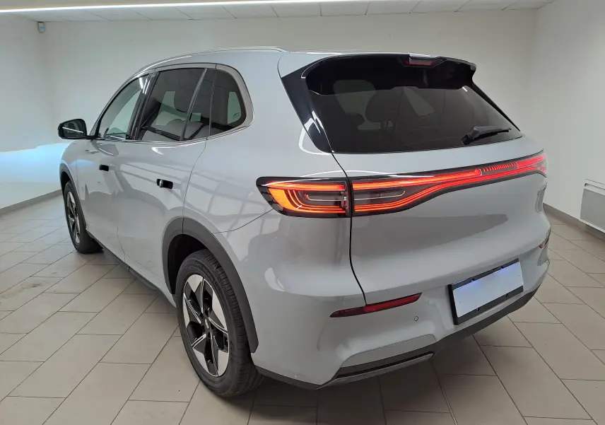 Vue 3/4 arrière droite du SUV électrique Geely E5 PRO gris Moonlight avec feux arrière LED allumés dans un intérieur neutre.