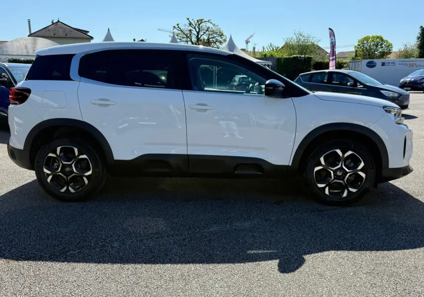 Profil côté droit d'un Citroën C5 Aircross blanc banquise avec jantes bi-ton et toit noir en extérieur.