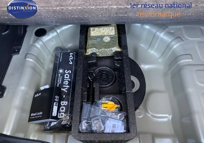 Coffre ouvert du Kia Stonic gris météore 2024 montrant rangement sous plancher avec kit de sécurité et outils.