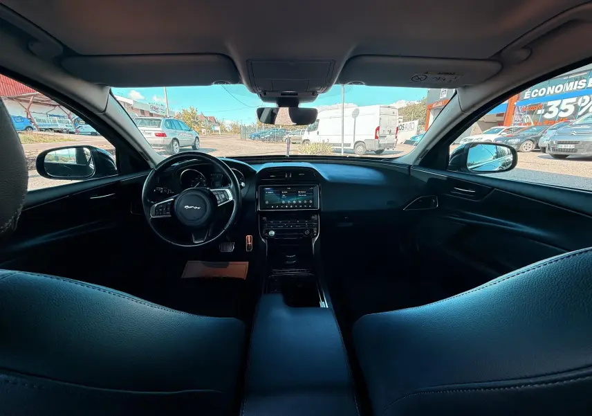 Vue intérieure avant de la Jaguar XE 2.0D 180CH Prestige 2019 avec tableau de bord et volant en cuir noir.