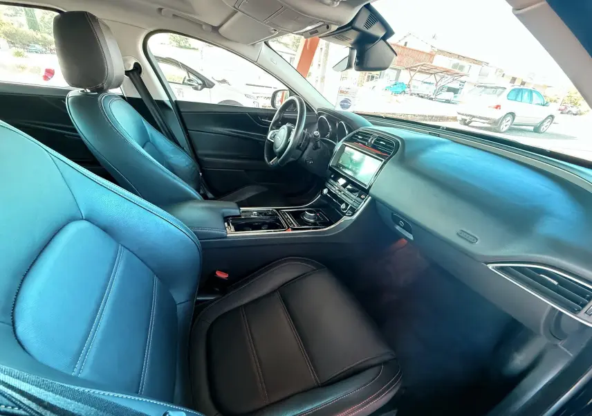 Intérieur avant droit d'une Jaguar XE 2019 avec sièges cuir noir et tableau de bord moderne équipé d'un écran tactile.