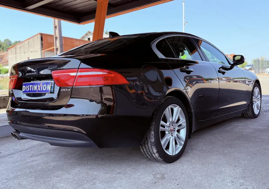 Vue 3/4 arrière droite d'une Jaguar XE noire brillante avec jantes argentées sous un abri extérieur.