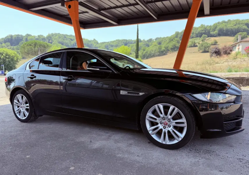 Jaguar XE noir vu de profil côté gauche sous un abri, avec jantes argentées et calandre distinctive.