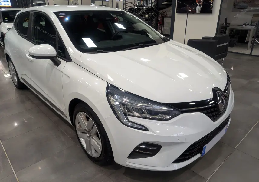 Renault Clio V blanc Glacier vue 3/4 avant droit, avec phares LED et jantes alliage en intérieur showroom.