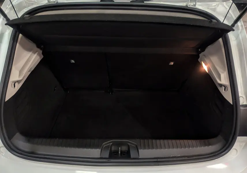 Coffre ouvert vu de l'arrière d'une Renault Clio V blanc glacier, intérieur noir avec éclairage latéral droit.