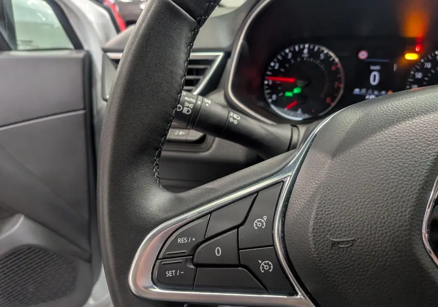 Gros plan sur le volant noir de la Renault Clio V blanc Glacier, mettant en valeur les commandes de régulateur de vitesse.