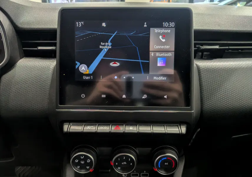 Vue rapprochée de l’écran tactile central et des commandes de climatisation d’une Renault Clio V blanche Glacier de 2020.