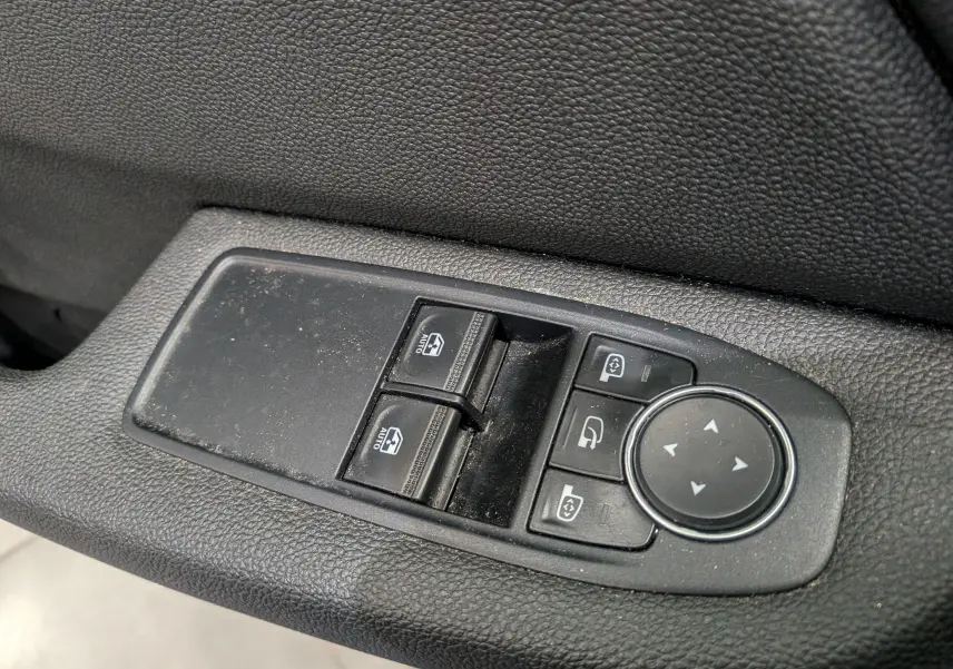 Gros plan sur les commandes de lève-vitres et réglage des rétroviseurs côté gauche d'une Renault Clio V blanche.