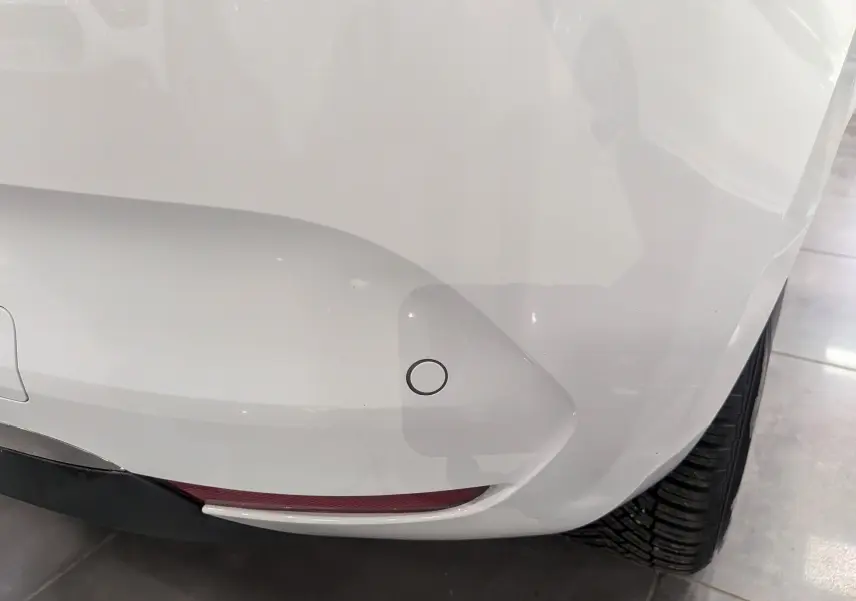 Gros plan sur le pare-chocs arrière droit blanc glacier d'une Renault Clio V TCe 100 CH X-TRONIC BUSINESS avec capteur de recul.