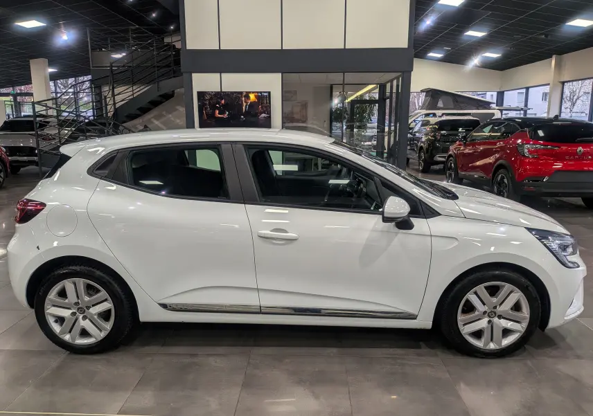 Profil côté gauche d'une Renault Clio V blanche Glacier, version TCe 100 CH X-TRONIC BUSINESS, en showroom lumineux.