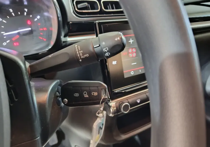 Détail intérieur du volant et du commodo de la Citroën C3 gris foncé, avec écran tactile et clé insérée.
