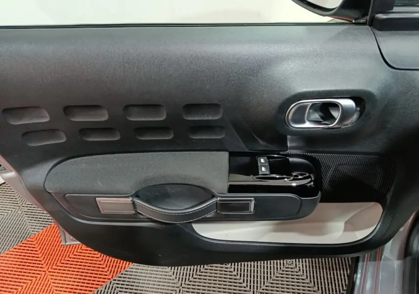 Détail de la porte côté conducteur d'une Citroën C3 gris foncé, avec poignée noire et commandes de vitres.