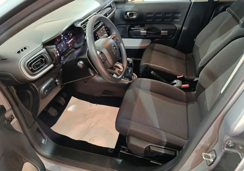 Vue intérieure côté conducteur de la Citroën C3 gris foncé 2024, volant multifonctions et sièges tissu gris.