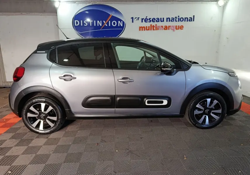 Profil droit d'une Citroën C3 gris foncé 2024 avec protections latérales noires et jantes bicolores dans un showroom.