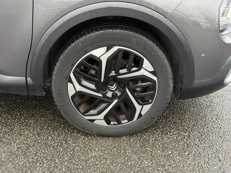 Gros plan sur la roue avant droite gris métallisé du Citroën C4 X 2024 avec jante alliage au design géométrique noir et argent.