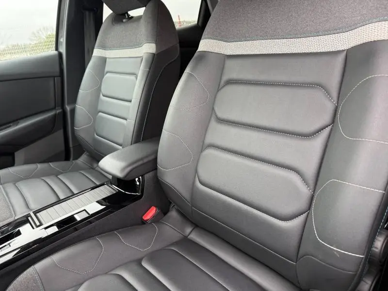 Vue rapprochée des sièges avant gris du Citroën C4 X 2024, mettant en valeur les finitions en tissu et cuir avec coutures apparentes.