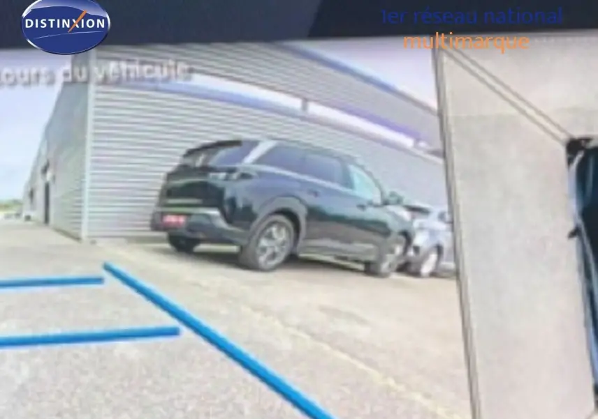 Vue 3/4 arrière d’un Peugeot 408 HYBRID 145CH GT noir métal stationné devant un bâtiment industriel.