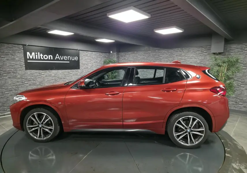 BMW X2 sDrive 18d M Sport orange métallisé vue de profil côté gauche en intérieur avec jantes 19 pouces M.