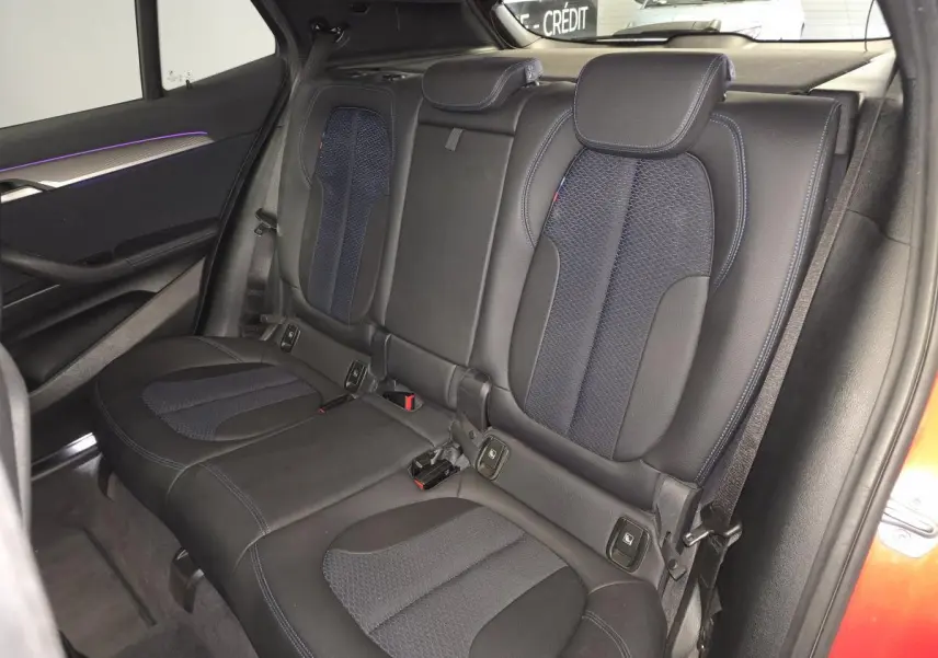 Vue intérieure de la banquette arrière du BMW X2 orange, avec sellerie tissu et similicuir noir et bleu, et inserts décoratifs.
