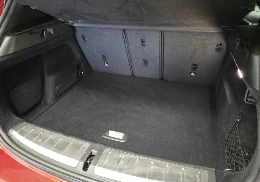 Coffre ouvert de BMW X2 orange, vue intérieure montrant tapis noir et filet de rangement latéral.