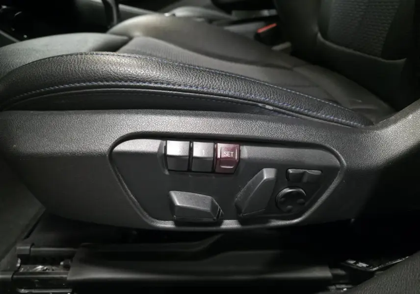 Gros plan sur les commandes électriques de réglage du siège conducteur en similicuir noir avec surpiqûres bleues d'une BMW X2 M Sport 2021.