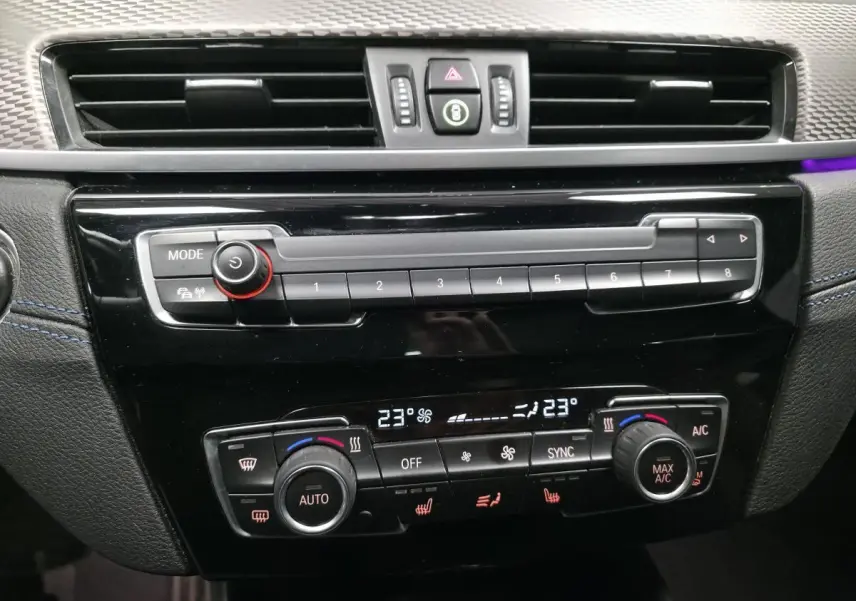 Vue rapprochée de la console centrale noire du BMW X2 avec commandes climatisation automatique bi-zone et autoradio.