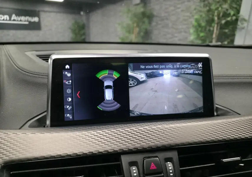 Écran central de BMW X2 orange montrant la caméra de recul et l’aide au stationnement en intérieur.