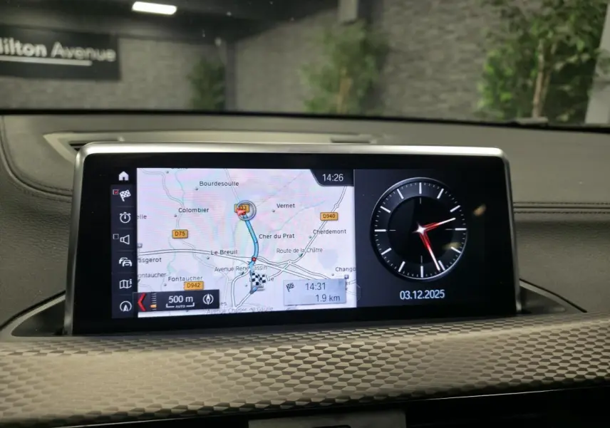 Écran central du tableau de bord BMW X2 M Sport 2021 affichant la navigation et une horloge digitale.