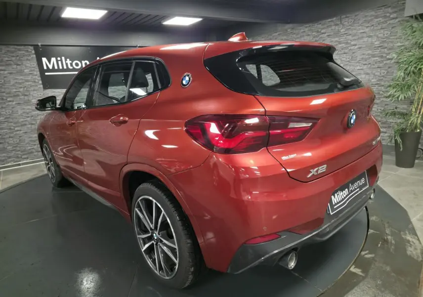 Vue 3/4 arrière droite d'une BMW X2 orange métallisée avec jantes alliage et double sortie d'échappement chromée.