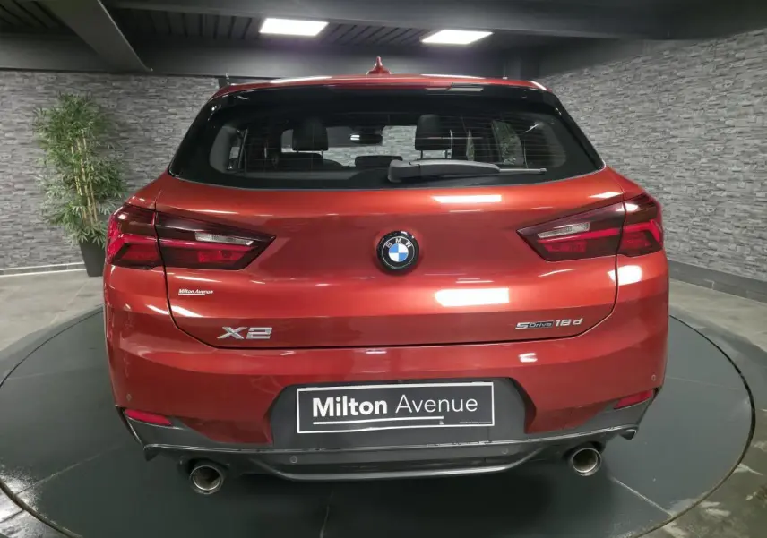 Vue arrière d'une BMW X2 sDrive 18d orange métallisée avec double sortie d'échappement et logo M Sport visible.