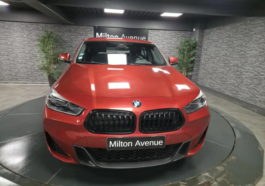 Vue avant d'une BMW X2 sDrive 18d M Sport orange métallisé avec calandre noire et plaque Milton Avenue.