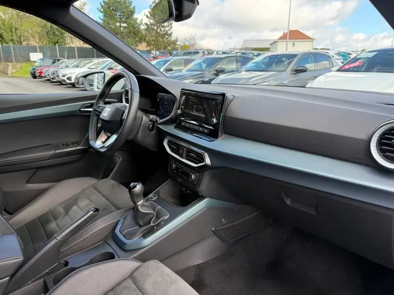 Intérieur du SEAT Arona 2025 vu côté conducteur, tableau de bord moderne avec écran tactile et levier de vitesse manuel.